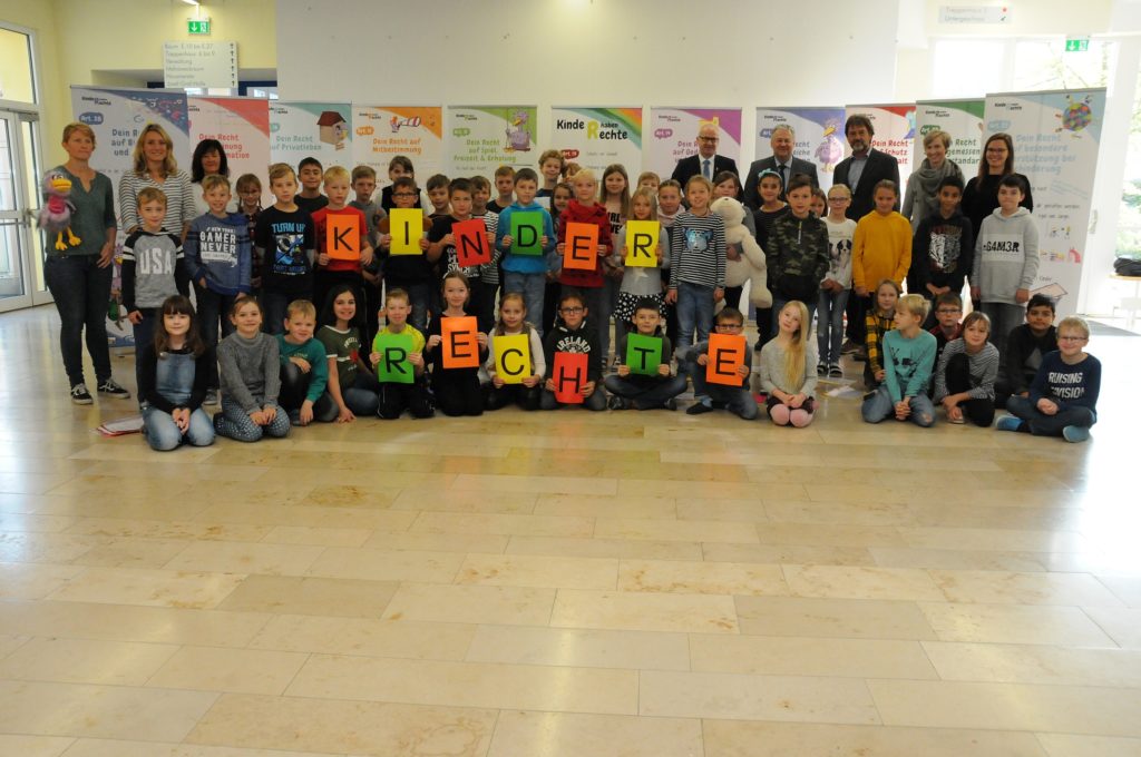 Gruppenfoto der Hahnbacher Grundschüler*innen mit Anita Kinscher, Claudia Mai (beide KoJa), Cornelia Bäuml (KJR), Bürgermeister Bernhard Lindner, Landrat Richard Reisinger, Rektor Heinz Meinl, sowie den Lehrerinnen Maria Liebig und Kerstin Schreglmann (hintere Reihe v.li.) vor den neu gestalteten Roll-ups zum Thema Kinderrechte. Foto: Christine Hollederer