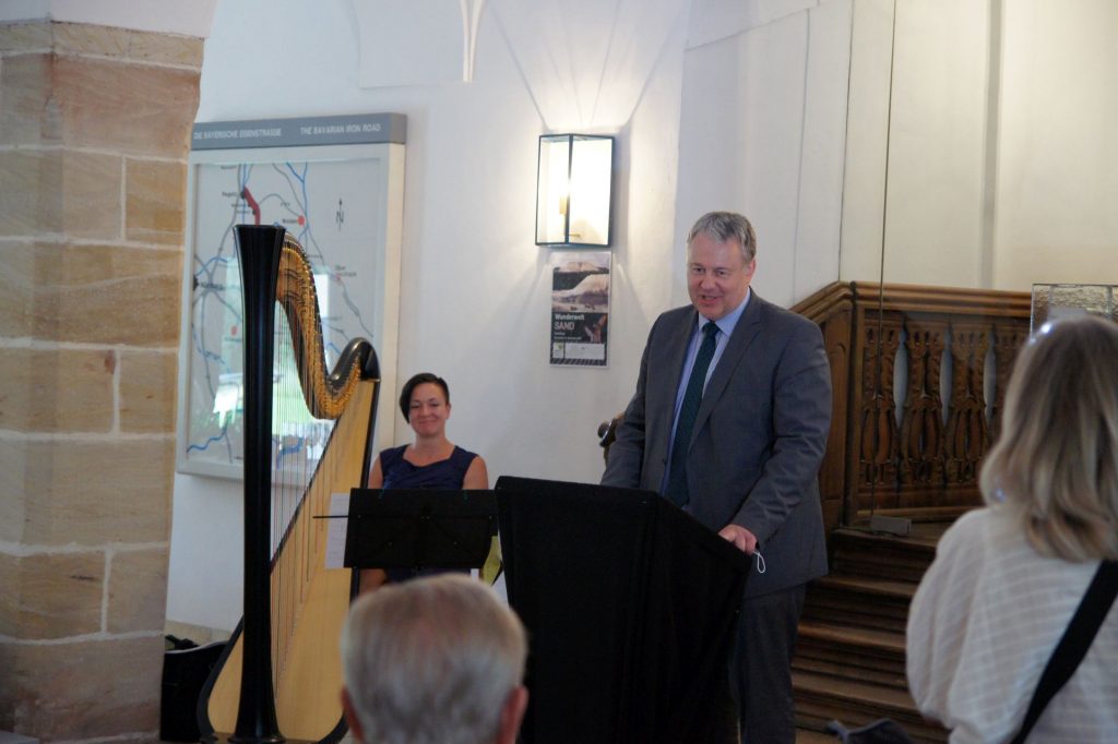 Landrat Richard Reisinger darf endlich wieder Besucher im Kultur-Schloss Theuern begrüßen. Diese lassen sich im Anschluss von der Ausstellung „Wunderwelt Sand“ faszinieren. An der Harfe ist Barbara Regnat.  Foto: Rita Kummer