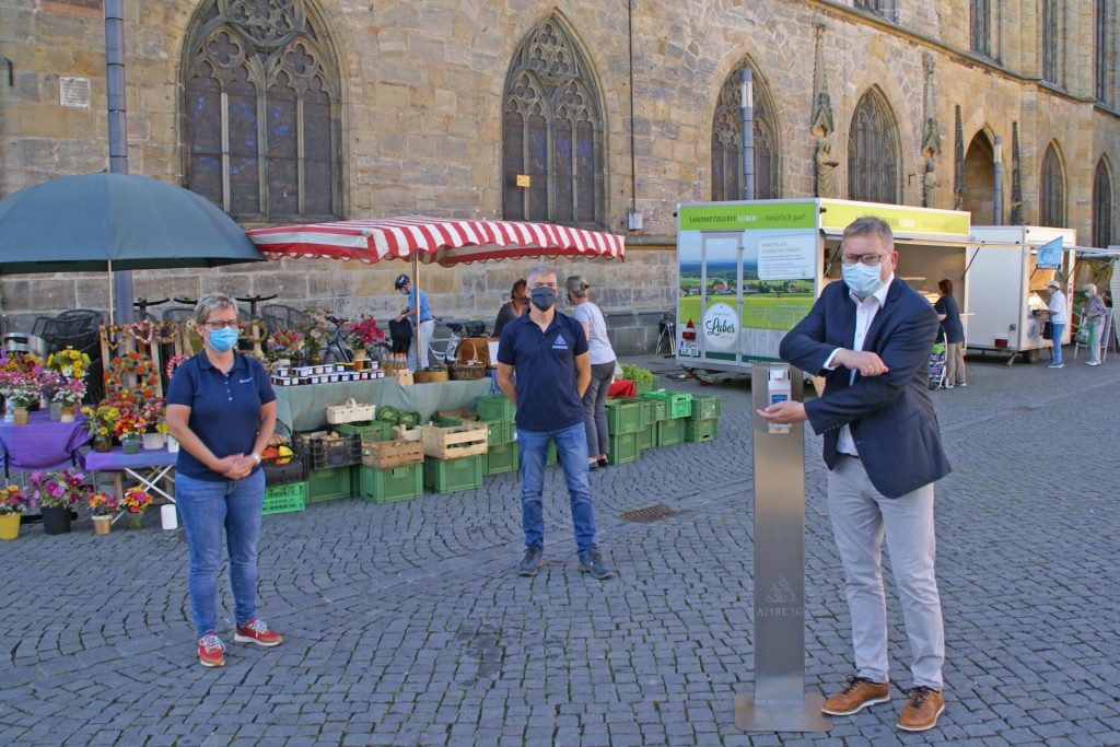 Oberbürgermeister Michael Cerny geht mit gutem Beispiel voran: Er nutzt mit Amtsleiterin Elisabeth Keck (links) und Lothar Thumbeck (mitte) vom Amt für Ordnung und Umwelt den Desinfektionsspender auf dem Marktplatz. Foto © Stadt Amberg, Ina Bogner