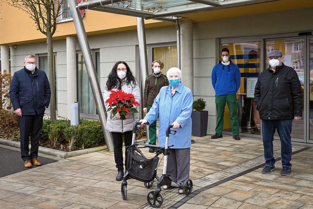 Oberbürgermeister Michael Cerny, Hauswirtschaftsleiterin Maria Bauer, die Auszubildenden der Stadtgärtnerei Nadine Domogalla und Christopher Hirteis sowie Gärtnereileiter Bernhard Richter (hinten v.l.n.r.) überreichen der Bewohnerin des Bürgerspitals Berta Götz (vorne) symbolisch einen von insgesamt 272 Weihnachtssternen, über die sich die Amberger Altenheimbewohner in diesem Jahr freuen können. Foto: Susanne Schwab, Stadt Amberg