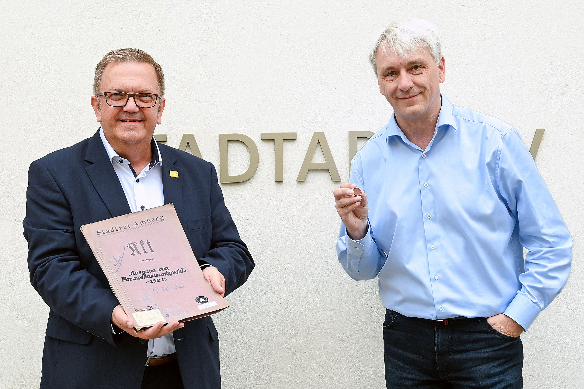 Ambergs Zweiter Bürgermeister Martin J. Preuß (links) und der Leiter des Stadtarchivs Dr. Andreas Erb mit der Amberger Porzellanmünze, die exakt vor 100 Jahren zum 500jährigen Jubiläum der Martinskirche produziert worden ist, und der Akte mit den dazugehörigen Schriftstücken. Foto: Susanne Schwab, Stadt Amberg