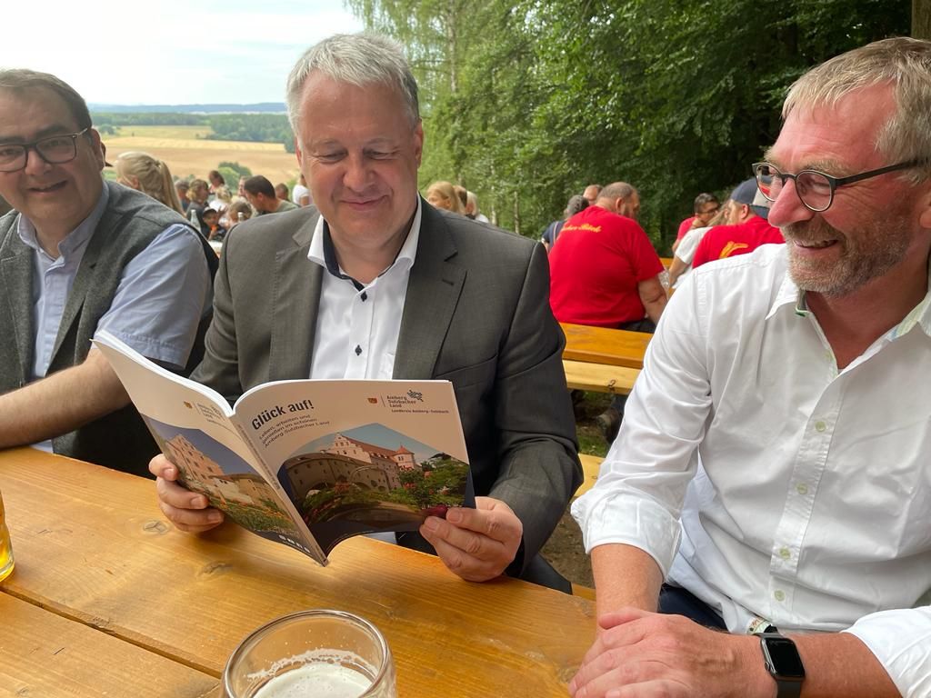 Zum Abschluss des Annaberg-Festes in Sulzbach-Rosenberg wirft Landrat Richard Reisinger (Mitte) einen interessierten Blick in die neue Broschüre. Auch Pfarrer Hubert Mader von der Pfarrei St. Marien und Pfarrgemeinderat Andreas Schober (von links) wünschen zum Landkreisjubiläum alles Gute und weiterhin „Glück auf“ Foto: Joachim Gebhardt