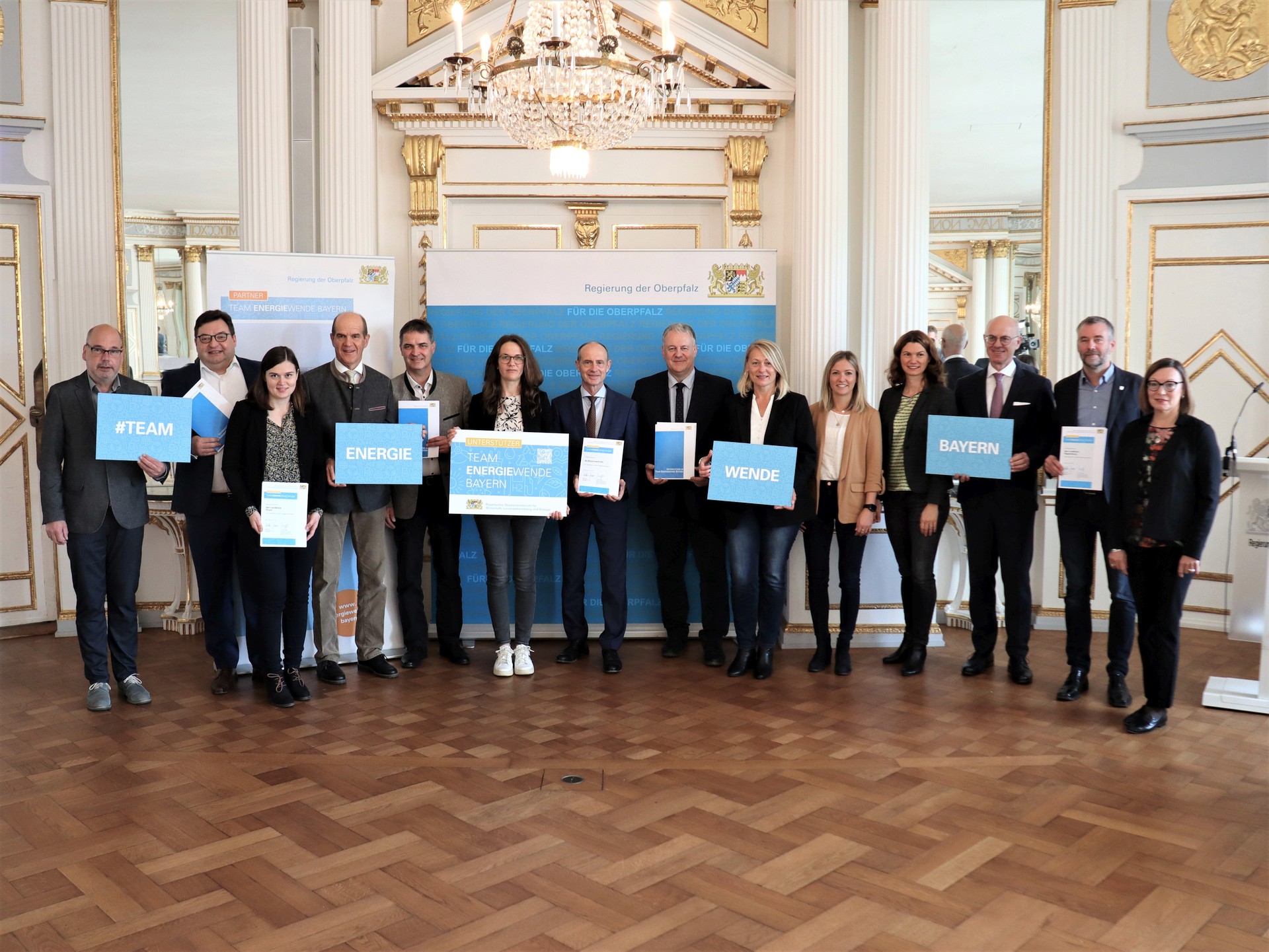 Regierungspräsident Walter Jonas (3.vr) zusammen mit den neuen Unterstützern im Team Energiewende Bayern (vlnr): Dr. Wolfgang Fruhmann, Aufsichtsratsvorsitzender Jurenergie e.G.. und Michael Vogel, Vorstand Jurenergie e.G., Klimaschutzmanagerin Sylvia Bauer vom Landkreis Cham, Regenstaufs 2. Bürgermeister und Vorsitzender des Klimabeirates Bruno Schleinkofer, Regenstaufs 1. Bürgermeister Josef Schindler, Regenstaufs Klimaschutzmanagerin Veronika Preis, Dr. Egon Westphal, Vorstandsvorsitzender Bayernwerk AG, Amberg-Sulzbachs Landrat Richard Reisinger, Yvonne Busch und Linda Trager vom Zentrum für erneuerbare Energien und Nachhaltigkeit e.V. im Landkreis Amberg-Sulzbach, Regensburgs Landrätin Tanja Schweiger, Niels Alter, Klimaschutzmanager des Landkreis Regensburg und Sigrun Denner vom Team Energiewende an der Regierung der Oberpfalz. Foto: Regierung der Oberpfalz/Schmied