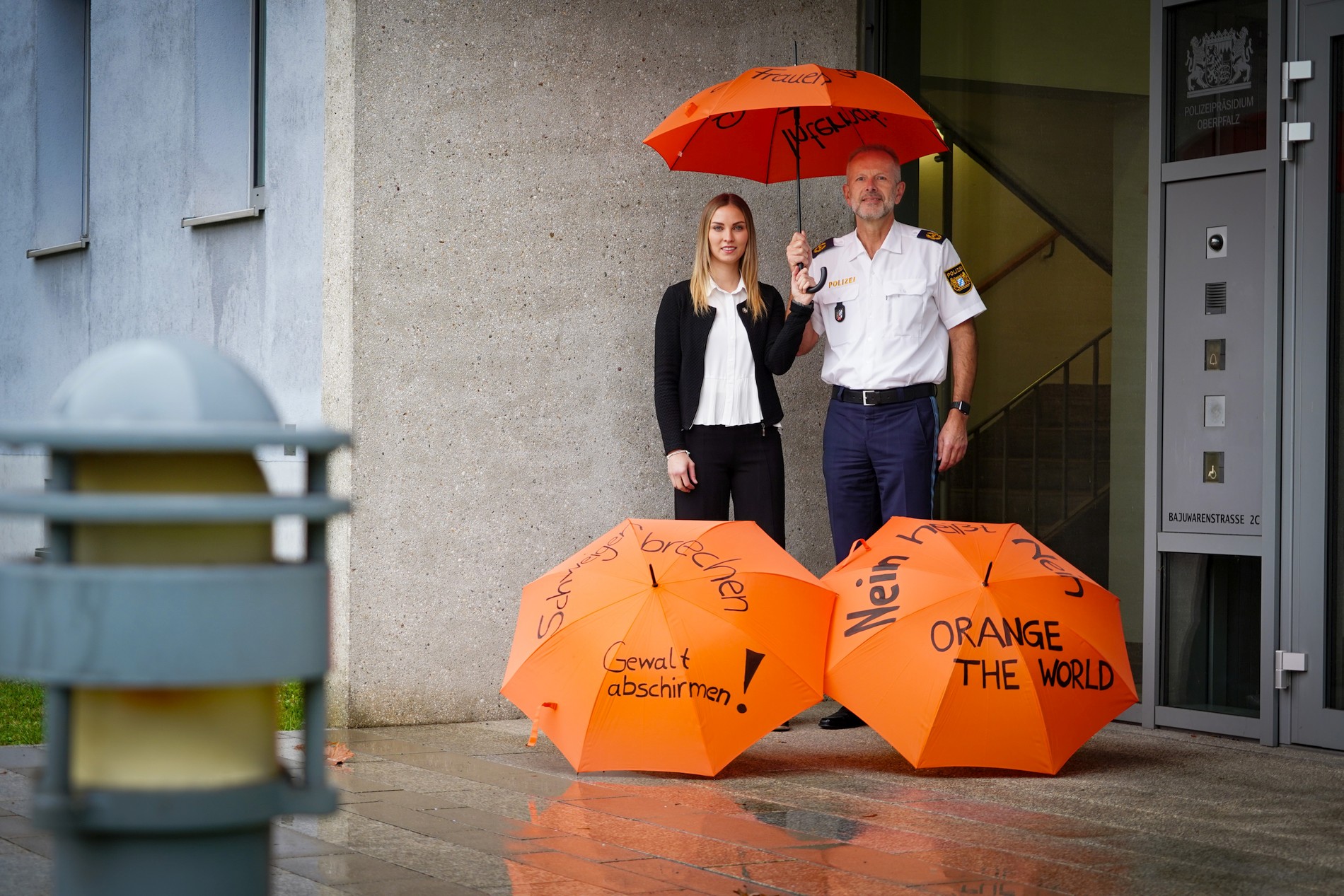 Die stellvertretende BPfK Kriminalhauptkommissarin Corinna Wild und Polizeivizepräsident Thomas Schöniger mit orangen Schirmen, die Botschaften gegen Gewalt an Frauen enthalten Foto: PP Oberpfalz/tw