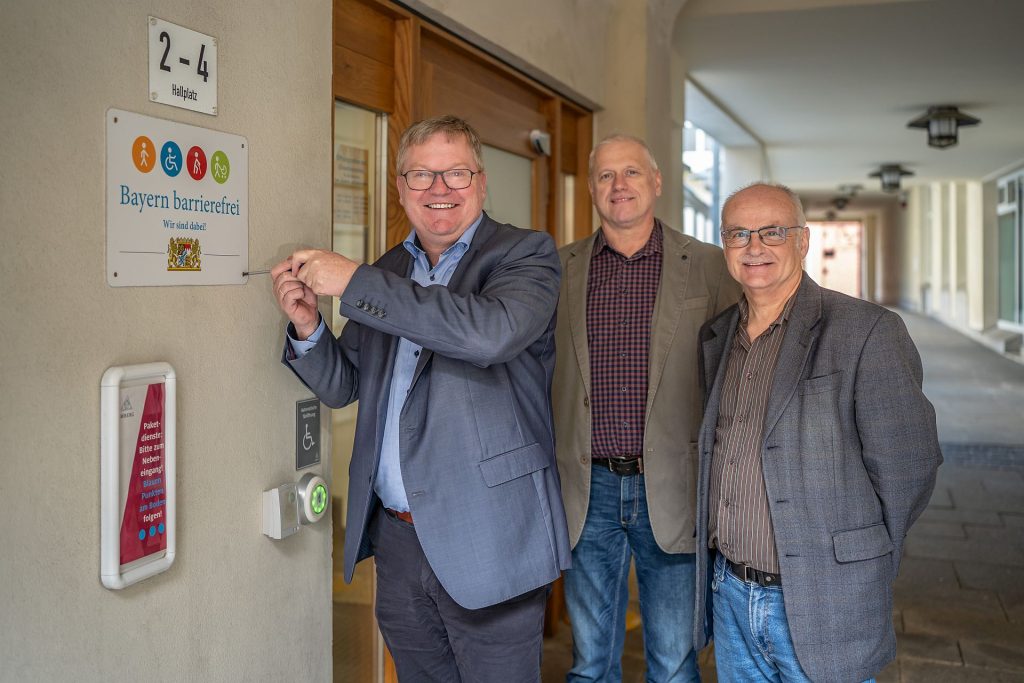 Oberbürgermeister Michael Cerny schraubt das Signet "Bayern barrierefrei" fest. Josef Singer, Leiter Zentrale Dienste (rechts), und Martin Kroher, Schwerbehindertenvertretung (mitte), freuen sich ebenfalls über die Auszeichnung. Foto Michael Golinski, Stadt Amberg